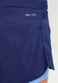 Laivaston siniset urheilushortsit, joissa on DRI-FIT-etiketti, hengittävää, rei'itettyä kangasta, kaareva helma ja sileä, kevyt rakenne.