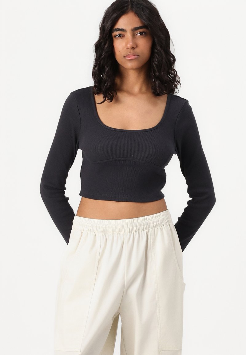 Crop top noir à manches longues en côtes avec un décolleté carré, associé à un pantalon crème à taille élastique. Texture lisse, design ajusté.