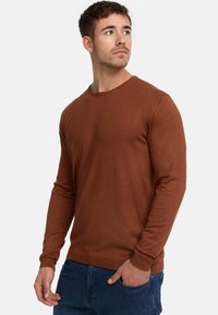 Braunes Langarmshirt aus gerippter Textur mit Rundhalsausschnitt, kombiniert mit blauen Jeans. Verfügt über enganliegende Bündchen und ein einfaches Design.