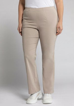 Pantalons beiges à jambe droite en tissu lisse, avec une taille haute, sans fermetures visibles, associés à des baskets blanches.