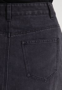 Černá denimová sukně s vysokým pasem, která má zadní kapsu, horizontální prošívání a čistý, strukturovaný povrch.