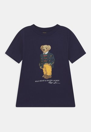 Marineblaue T-Shirt mit einer Grafik eines Bären, der eine grüne Jacke, einen gestreiften Pullover, gelbe Hose und braune Schuhe trägt, mit dem Text Polo Bear darunter.