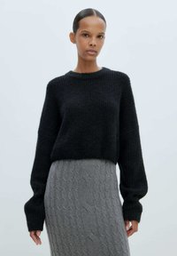 Schwarzer gestrickter Pullover mit rundem Ausschnitt und oversized �Ärmeln, kombiniert mit einem strukturierten grauen Zopfmuster-Rock.