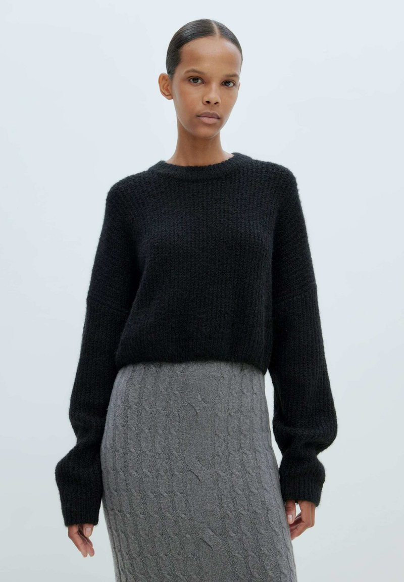 Schwarzer gestrickter Pullover mit rundem Ausschnitt und oversized Ärmeln, kombiniert mit einem strukturierten grauen Zopfmuster-Rock.