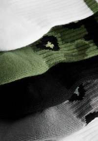 Trzy pary skarpetek: jedna biała, jedna w zielony kamuflaż z czarnymi akcentami, jedna czarna i szara ze wzorami. Wykonane z dzianiny o ribbowanej teksturze.