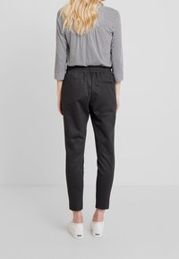 Zwart-witte geruite blouse met driekwartmouwen, gecombineerd met zwarte tapered broek, voorzien van een elastische tailleband en witte sneakers.