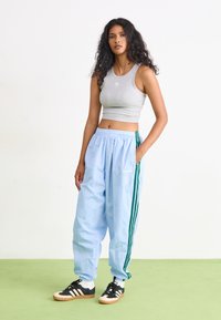 Hallikas crop-top, helesinised sportlikud püksid roheliste triipudega ja mustad spordijalatsid. Pehme kangas, lahti sobivus ja elastne vöökoht.