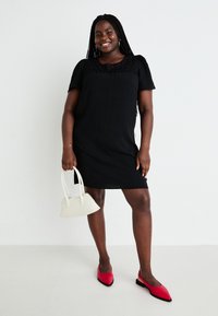 Vestito nero a maniche corte con dettagli in pizzo sul colletto, abbinato a ballerine rosse con punta e una piccola borsa bianca. Tessuto liscio.