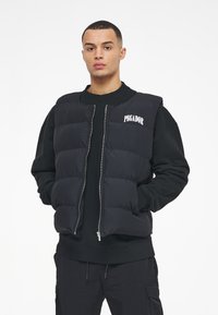 Black puffer vest with a zip front and an embroidered "PEGADOR" logo. Features quilted panels and a high neck design. Worn over a black sweatshirt.