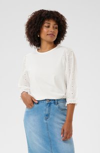 White t-shirt with textured, lace-like puff sleeves, paired with a light blue denim skirt. Notable details include fitted design and ruffled sleeve edges.