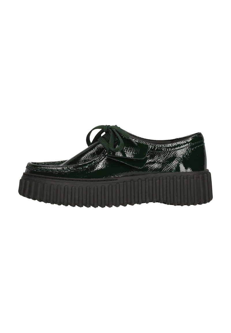 Zapato de charol verde con punta redondeada, diseño plano de cordones y suela gruesa negra estriada. Presenta una textura lisa y brillante.