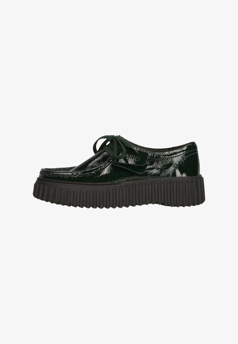 Zapato de charol verde con punta redondeada, diseño plano de cordones y suela gruesa negra estriada. Presenta una textura lisa y brillante.