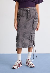 Hame midi denim harmaa, jossa on cargo-taskut, raaka helma ja naru-sivut, yhdistettynä valkoisiin sukkiin ja punaisella korostetuihin urheilukenkiin.