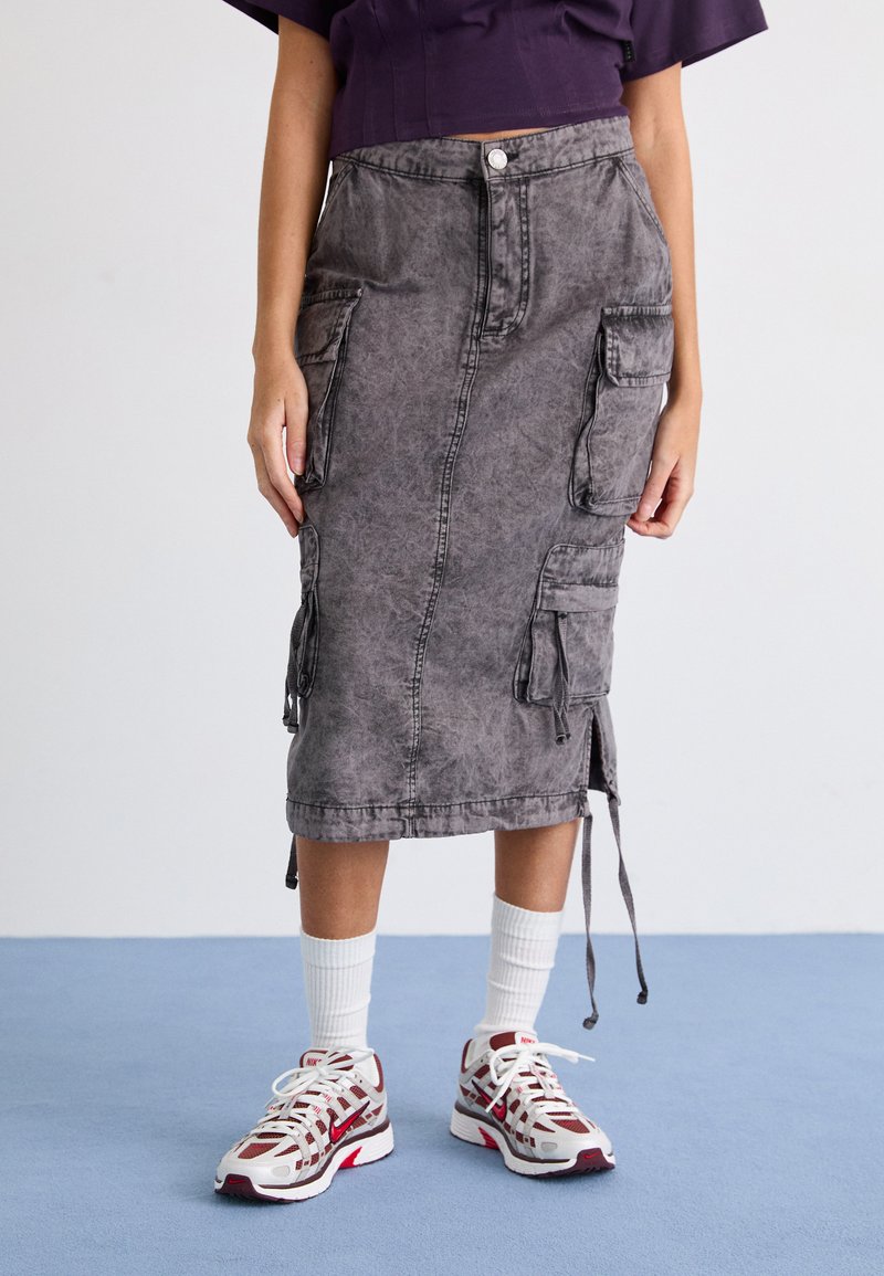 Hame midi denim harmaa, jossa on cargo-taskut, raaka helma ja naru-sivut, yhdistettynä valkoisiin sukkiin ja punaisella korostetuihin urheilukenkiin.