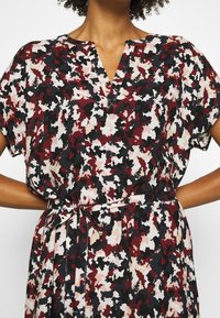Vestido con estampado floral en burdeos, negro y crema. Presenta un escote en V, mangas cortas y una cintura ajustada para una silueta definida.
