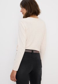 Ljusrosa långärmad skjorta i kombination med svarta jeans. Skjortan har en enkel design, medan jeansen har bakfickor och detaljer i form av band.