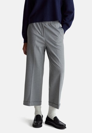 Pantalon gris à coupe décontractée avec une taille élastique et une jambe large. Présente une texture lisse et un ourlet replié, associé à des mocassins noirs et des chaussettes blanches.