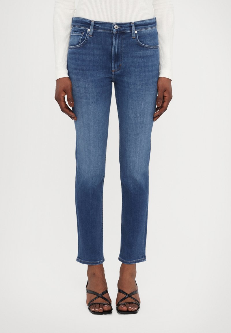 Medium wash denim jeans met een rechte pijp, vijf zakken en subtiele vervaging. Gepaard met zwarte sandalen met bandjes.