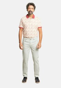 Camisa polo para hombre con un estampado floral en colores pastel, cuello y puños rojos, combinada con pantalones claros y zapatos negros.