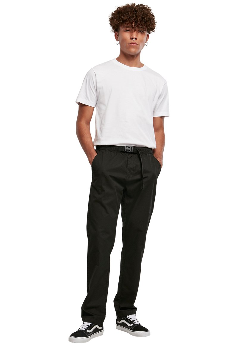 Sorte bukser med elastisk liv, sidelommer og en afslappet pasform, parret med en ensfarvet hvid T-shirt med korte ærmer og sorte sneakers.