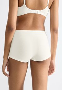 Ljusbeige bomullsunderkläder med hög midja, med en slät yta och minimal sömnad, som visar en enkel och funktionell snitt.