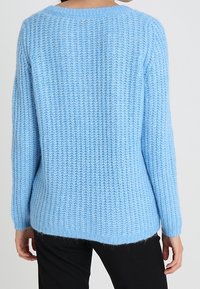 Ljusblå, strukturerad stickad tröja med avslappnad passform, rund halsringning och långa ärmar, med en diskret logotypetikett på baksidan.