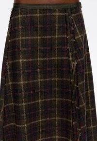 Detailný záber na tmavozelenú a námorníckom modrom károvanom kilte s červenými a béžovými pruhmi, nosený v páse, s viditeľnou textúrou látky a záhybmi.