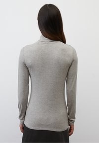 Graues Langarmoberteil mit enganliegendem Design, hohem Kragen und weicher Textur, kombiniert mit einem dunklen, fließenden Rock.