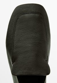 Chaussure en cuir noir avec une surface lisse et texturée et un bout arrondi. Présente une couture minimale et un design à enfiler sans aucune quincaillerie visible.