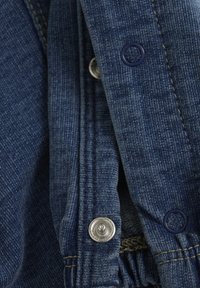 Jeanstyg i mörkblått med en texturerad yta. Har silverfärgade tryckknappar och marinblå accentknappar vid öppningen. Fint stygn detaljer.