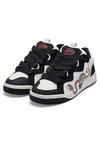 Black and white sneakers with thick black laces, featuring a snake graphic and red emblem on the tongue, textured black rubber sole.