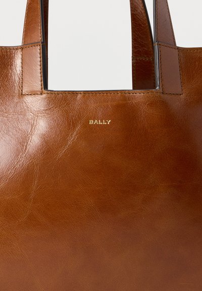 Καφέ δερμάτινη τσάντα με δύο λουριά και χρυσό λογότυπο "BALLY" ανάγλυφο στο κέντρο μπροστά.