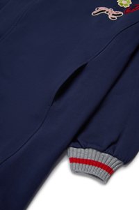 Mørkeblå sweatshirt med ribbestrikkede grå mansjetter med røde striper, dekorative lapper i forskjellige farger og detalj ved sidesømmen.
