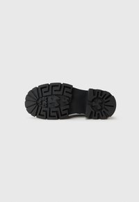 Talpa de pantof din cauciuc negru cu un model de profil pronunțat, prezentând un design geometric și accente ridicate, texturată pentru aderență și durabilitate.