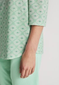 Maglietta da loungewear verde menta con un motivo floreale in bianco e viola chiaro, dotata di maniche a tre quarti e una texture di tessuto morbido.