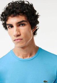 Camiseta de algodón azul claro con cuello redondo y un pequeño logotipo bordado en la parte izquierda del pecho. Textura suave y diseño ajustado.
