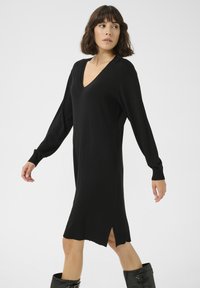 Schwarzes, langärmliges Kleid mit V-Ausschnitt, seitlichen Schlitzen und gerippten Bündchen. Hergestellt aus einem weichen Material mit einer lockeren Passform, eignet sich für verschiedene Anlässe.