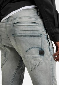 Ljusgrå denimjeans med flera fickor, kontrasterande sömmar och en svart etikett på bakfickan. Slät textur med en urtvättad finish.