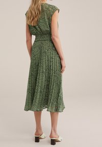 Abito midi verde a fantasia con vita smock, maniche a cappuccio e orlo fluido; abbinato a mules con tacco a blocco crema.