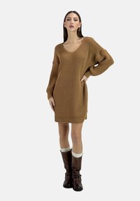 Brown knitted sweater dress with a V-neck and long, wide sleeves, complemented by knee-high brown boots and cream-colored socks.