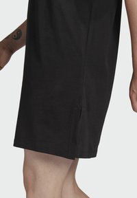 Svart bomullst-shirt klänning, knä-lång, med sidoklipp för rörlighet. Korta ärmar, rund halsringning, mjuk textur, avslappnad design.