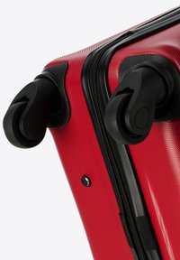Roter Hartschalenkoffer mit strukturierter Oberfläche, schwarzen Rollen und Reißverschluss. Verfügt über einen metallischen Knopf und robuste Griffbefestigungen.