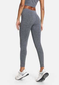 Szare, teksturowane legginsy z wysokim paskiem, dopasowanym krojem i bezszwowym wzorem, połączone z białymi butami sportowymi.