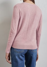 Ljusrosa tröja i mjukt material med en strukturfinish, ribbade ärmslut och nederkant, bärs tillsammans med blå denimjeans.