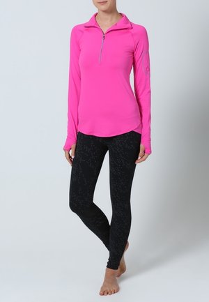 Figursydd långärmad topp i rosa med en kvartszipskrage, kombinerad med svarta leggings med prickigt mönster. Mjukt, stretchigt tyg.