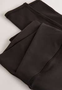 Leggings neri realizzati in un materiale liscio ed elastico. Presentano cuciture rinforzate e un design aderente, piegati ordinatamente e sovrapposti.
