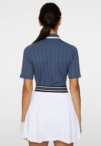 Mörkblå ribbad polo med korta ärmar, kombinerad med en vit plisserad kjol som har ett midjeband med svart och vit rand.