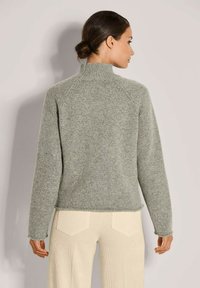 Grauer Strickpullover mit hohem Kragen, Raglanärmeln und gerippten Bündchen. Weiche Textur, lockere Passform und leicht verkürztes Design.