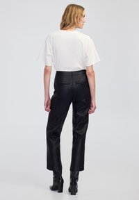 Czarne skórzane spodnie z dwoma tylnymi kieszeniami, zestawione z luźną białą koszulą. Modelka ma na sobie czarne botki na obcasie.