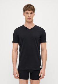 Schwarzes kurzärmliges T-Shirt mit V-Ausschnitt, aus glattem Stoff gefertigt. Mit einem weißen Adidas-Logo auf der unteren linken Seite.